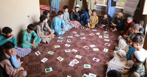 Group of young afghan boys sitting in a circle on the floor participating in a workshop